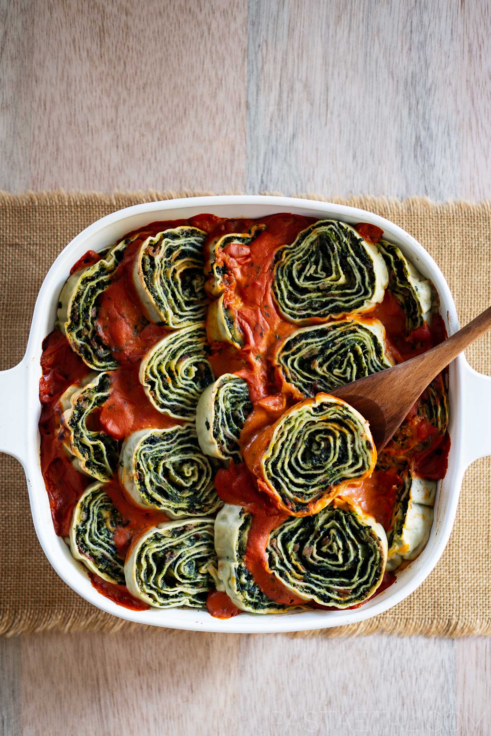 https://pastaetal.com/wp-content/uploads/2020/12/spinach-and-ricotta-rotolo-pasta-with-tomato-and-bechamel-sauce-in-a-baking-dish-with-a-wooden-spoon.jpg